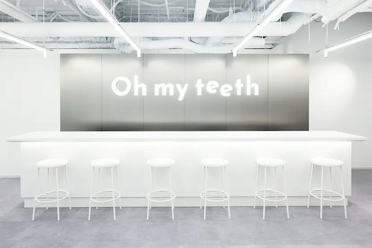 Oh my teeth札幌店のウェイティングエリア:「Oh my teeth」ロゴ入りウォールと白いスツールの並ぶカウンター