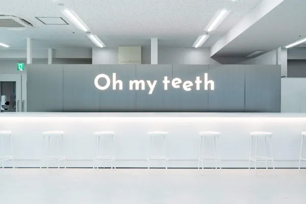 Oh my teeth梅田店のウェイティングエリア:「Oh my teeth」ロゴ入りウォールと白いスツール