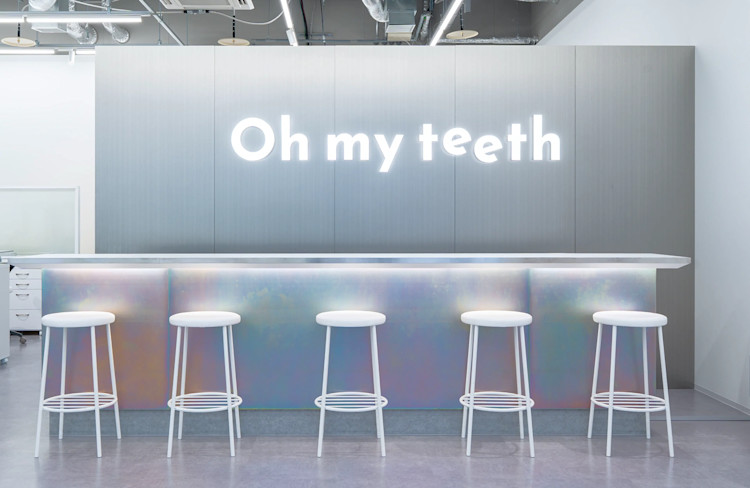 Oh my teeth広島店のウェイティングエリア:「Oh my teeth」ネオンサインとホログラフィックなカウンターと白いスツール
